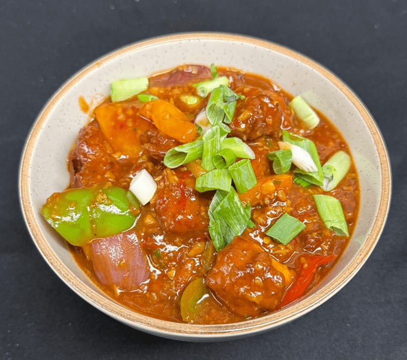 A bowl of Manchurian with bell peppers, onions, and scallions in a rich sauce.