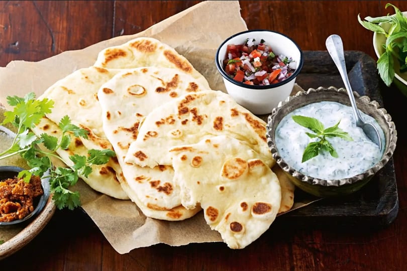 Freshly baked naan bread with cilantro, salsa, and a bowl of tzatziki sauce.