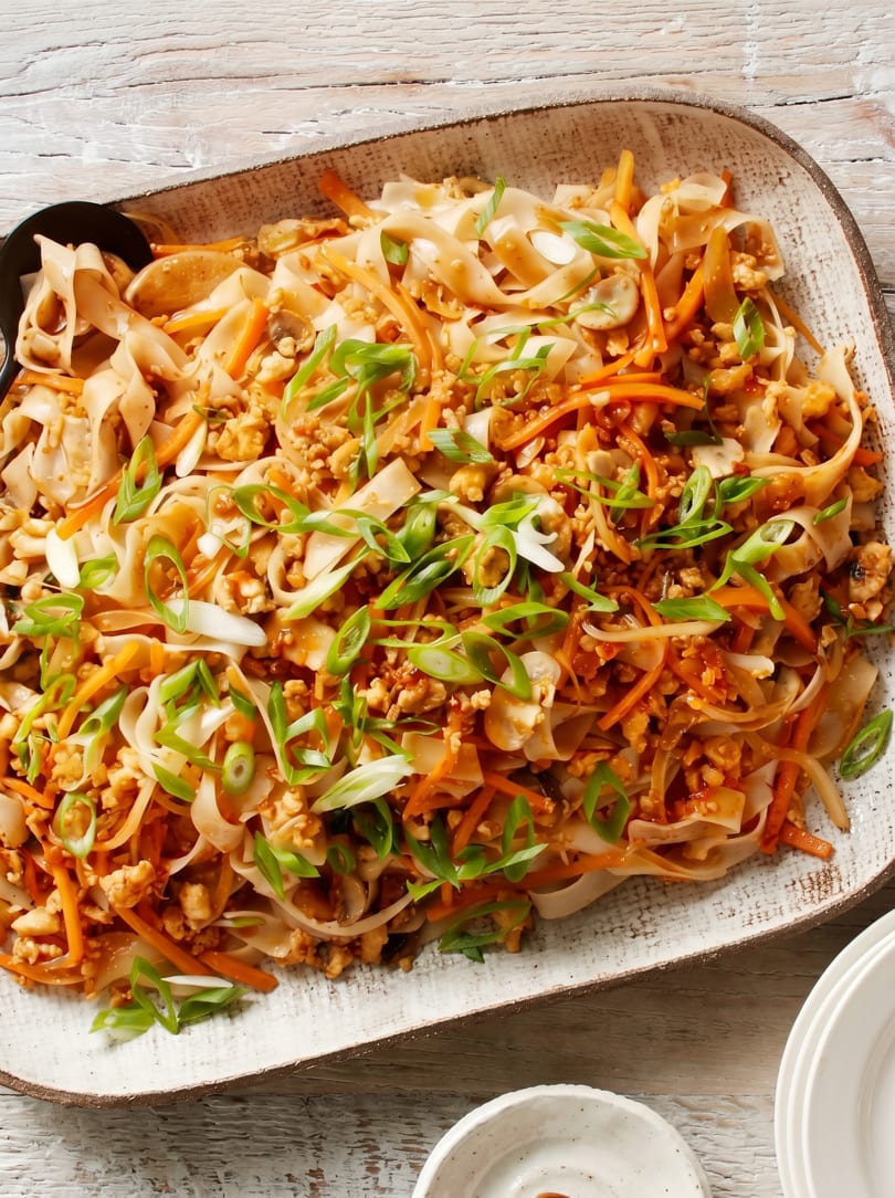 A large platter of Pad See Ew noodles with chicken, carrots, mushrooms, and green onions.