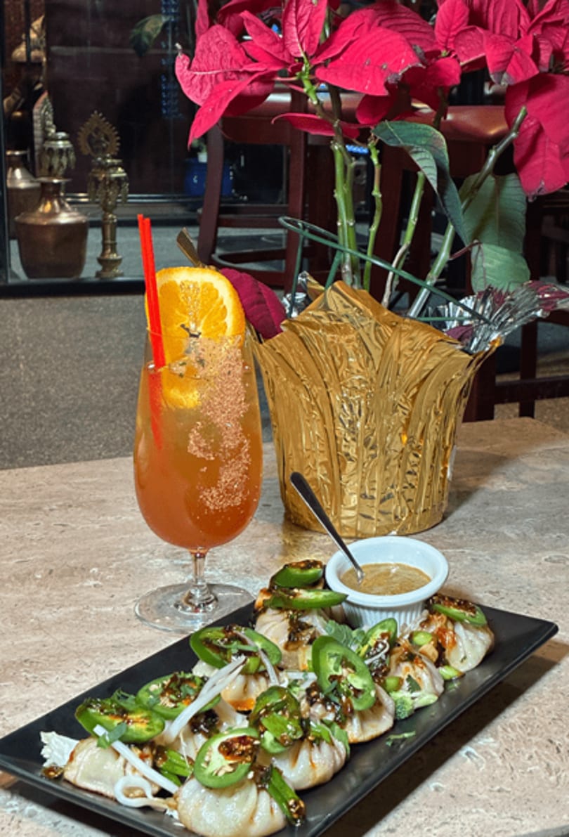Dumplings topped with jalapeños and sauce, a cocktail, and a poinsettia plant on a table.