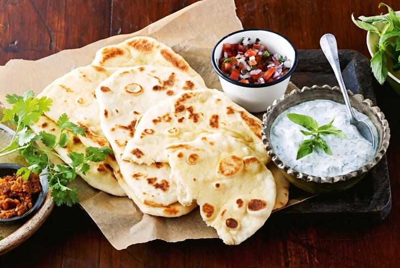 Naan bread with cilantro, salsa, and a bowl of tzatziki sauce on a wooden table.